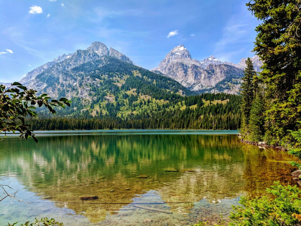 Taggart Lake with crystal-clear alpine water, forest shoreline, and Grand Teton peaks reflected across the lake — hike-to elopement location in Wyoming.