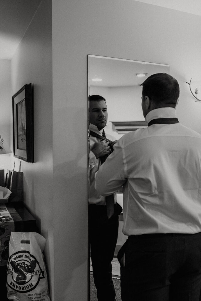 Groom adjusting jacket in cozy Inn on the Creek suite before winter Jackson Hole ceremony