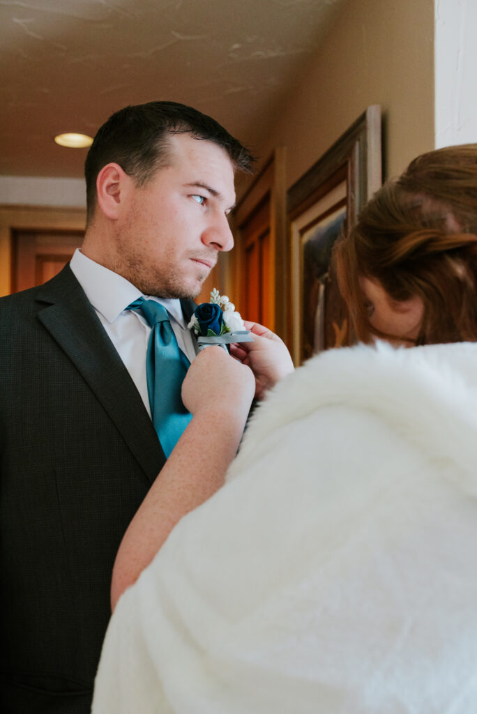 Bride pinning boutonniere at Inn on the Creek in Jackson Hole during a winter elopement