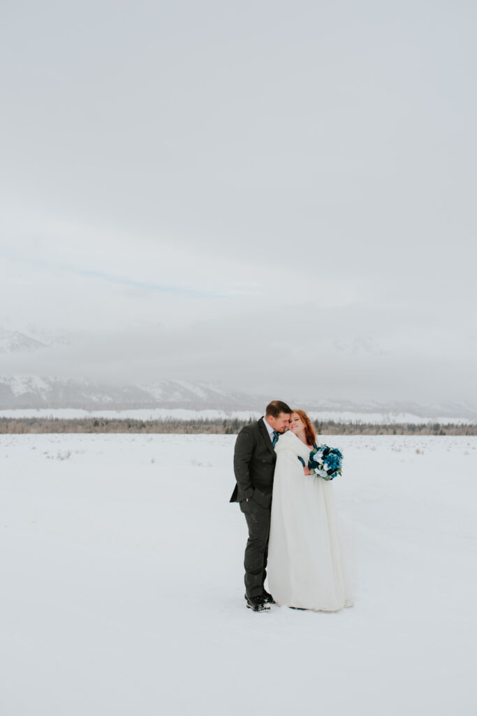 Couple embracing during a winter Jackson Hole elopement with snow-covered Tetons in the background