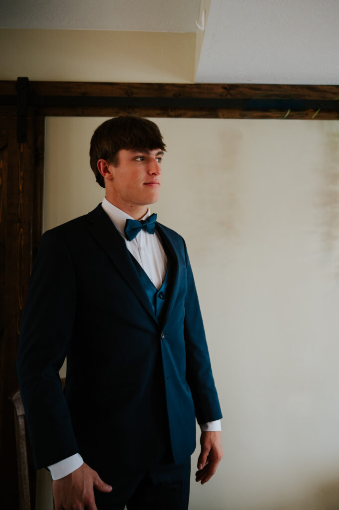 Groom getting ready for a Barn on 1st wedding in Idaho Falls adjusting suit jacket indoors